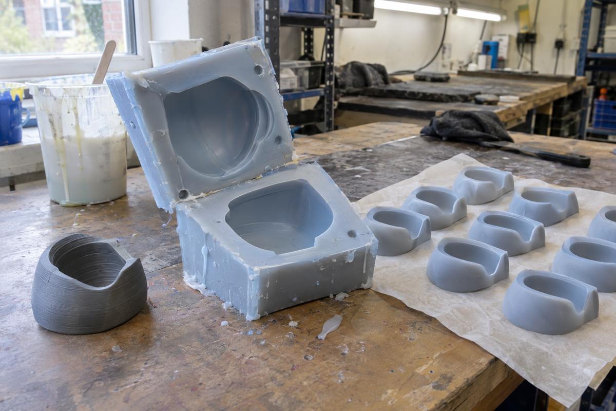 Hand-cast silicone tool with early kitchen accessory prototypes beside a printed master